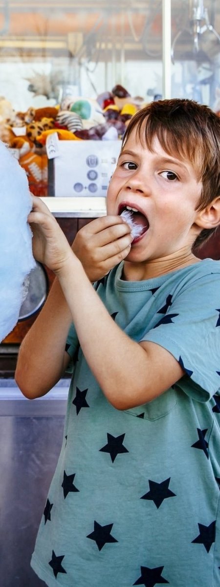 Photo of a brother and sister eating a big cotton candy at an amusement park.