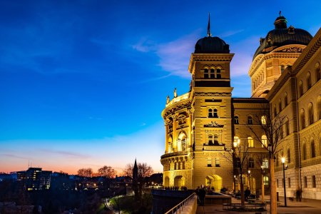 Das Bundeshaus, der Regierungssitz in Bern, hoch ber der Aare gelegen, wird zur Blauen Stunde golden angestrahlt.