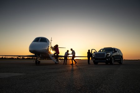 A young Asian pilot welcomes passengers into private jet at dusk.