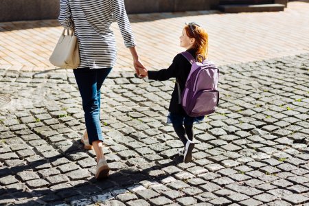 Crossing the street. Amazing little female keeping rucksack on her back while going to school