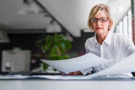 A photo of mature businesswoman examining documents at desk. Concentrated professional is analysing papers in office. Executive is in formals.