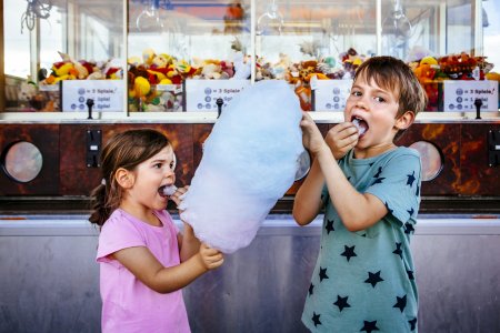 Photo of a brother and sister eating a big cotton candy at an amusement park.
