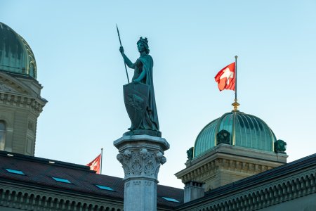 In the background the dome of the Bundeshaus the government building of Switzerland and the Swiss flag in the wind. 02/21/2021 - Bundesgasse, 3011 Bern, Canton Bern, Switzerland