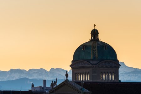View of the roof and dome of the Federal Palace in Bern. the snow-capped mountains of the swiss alps, in the background in the golden hour just before sunrise. 02/21/2021 - Parkterasse, 3012 Bern, Canton Bern, Switzerland