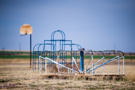 Horizontal image of abandoned playground. Basketball goal, Monkey bars and Merry-Go-Round against blue sky.