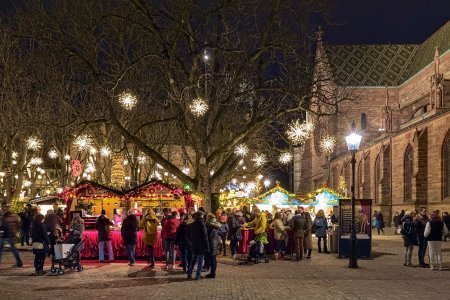 Basel, Switzerland - December 14, 2019: Christmas market at Munsterplatz square close to Basel Minster in dusk. Unknown people stand close to market stalls.