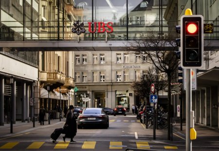 A woman crosses a road as logos of the Swiss banks Credit Suisse and UBS are displayed on buildings in Zurich, Switzerland on Saturday, March 18, 2023. (KEYSTONE/Michael Buholzer).