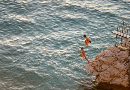 Teenagers having fun jumping from a cliff in to the sea