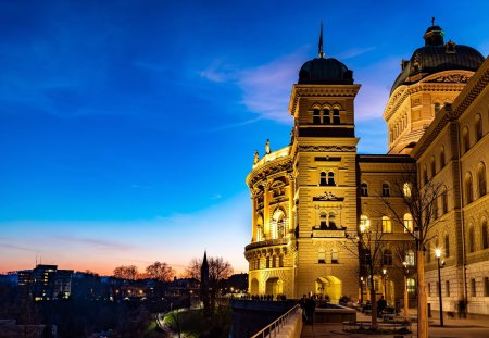 Das Bundeshaus, der Regierungssitz in Bern, hoch ber der Aare gelegen, wird zur Blauen Stunde golden angestrahlt.