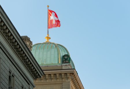 the flag waving in the wind above one of the domes of the Bundeshaus building. 02/21/2021 - Bundesplatz, 3011 Bern, Canton Bern, Switzerland
