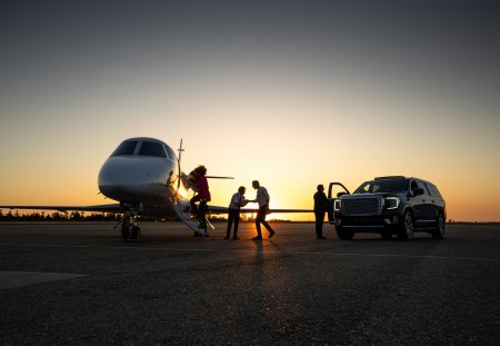 A young Asian pilot welcomes passengers into private jet at dusk.