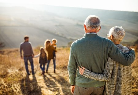 Back view of embraced grandparents enjoying while looking at their family on a field in autumn day.