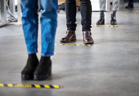 Low angle shot of business people standing behind social distancing signage on office floor. People in queue at office for safe entry checks post corona virus pandemic.