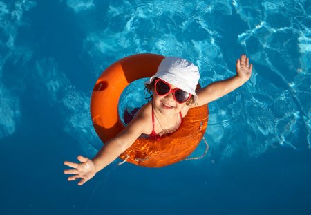 Funny little girl swims in a pool in an orange life preserver