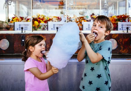 Photo of a brother and sister eating a big cotton candy at an amusement park.