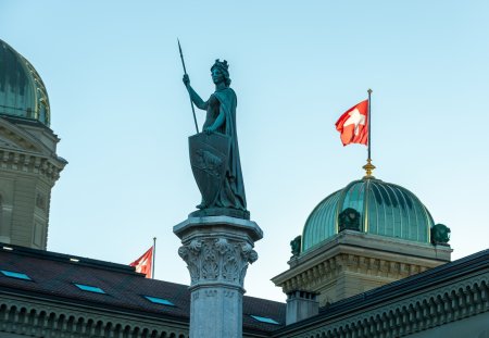 In the background the dome of the Bundeshaus the government building of Switzerland and the Swiss flag in the wind. 02/21/2021 - Bundesgasse, 3011 Bern, Canton Bern, Switzerland