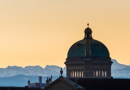 View of the roof and dome of the Federal Palace in Bern. the snow-capped mountains of the swiss alps, in the background in the golden hour just before sunrise. 02/21/2021 - Parkterasse, 3012 Bern, Canton Bern, Switzerland