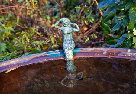 little mermaid sitting on the edge of a basin with reflection in the water