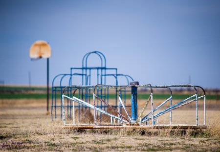 Horizontal image of abandoned playground. Basketball goal, Monkey bars and Merry-Go-Round against blue sky.