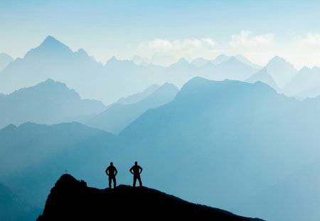 Two Happy winning successful silhouette hiker or climber at sunrise standing relaxed and are happy for having reached mountain top summit goal during alpine hiking and climbing adventure travel. Tirol, Austria and Allgaeu, Bavaria, Germany. Mountain Grosse Schlicke.