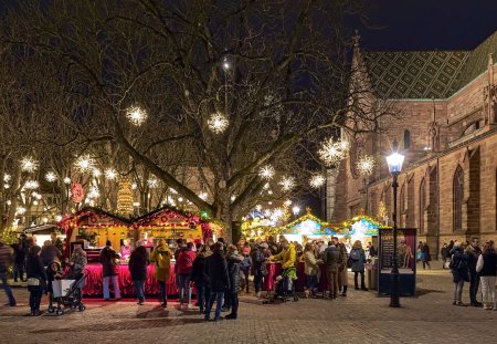 Basel, Switzerland - December 14, 2019: Christmas market at Munsterplatz square close to Basel Minster in dusk. Unknown people stand close to market stalls.