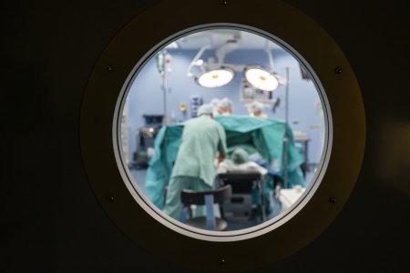 Blurred view into an operating theatre through a porthole in a door in a hospital with unrecognisable people.