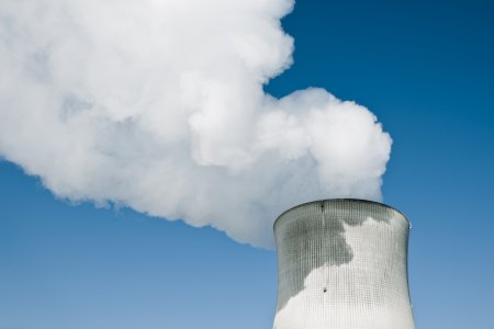 Nuclear Power Station with steaming tower over clear blue sky.