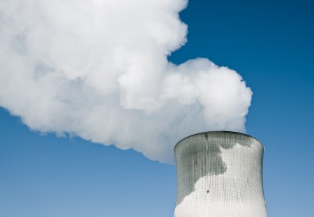 Nuclear Power Station with steaming tower over clear blue sky.