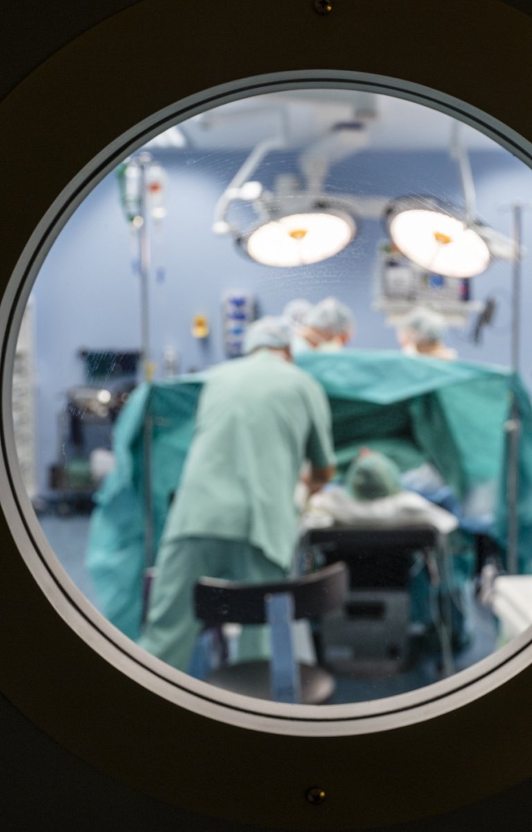 Blurred view into an operating theatre through a porthole in a door in a hospital with unrecognisable people.