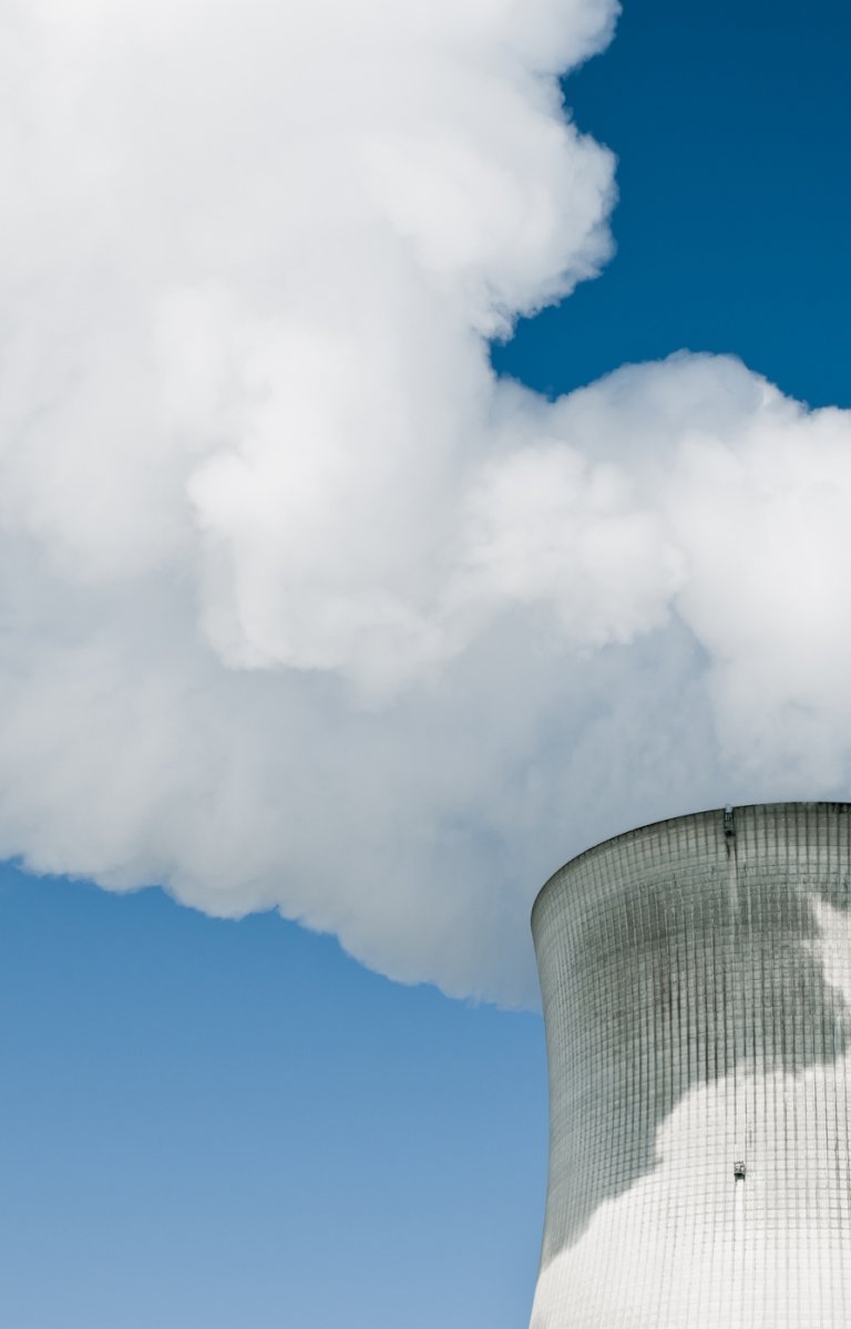 Nuclear Power Station with steaming tower over clear blue sky.
